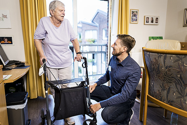 Situation im Pflegeheim: Eine alte Frau mit Gehhilfe und ein j&uuml;ngerer Mann mit Namensschild im Gespr&auml;ch